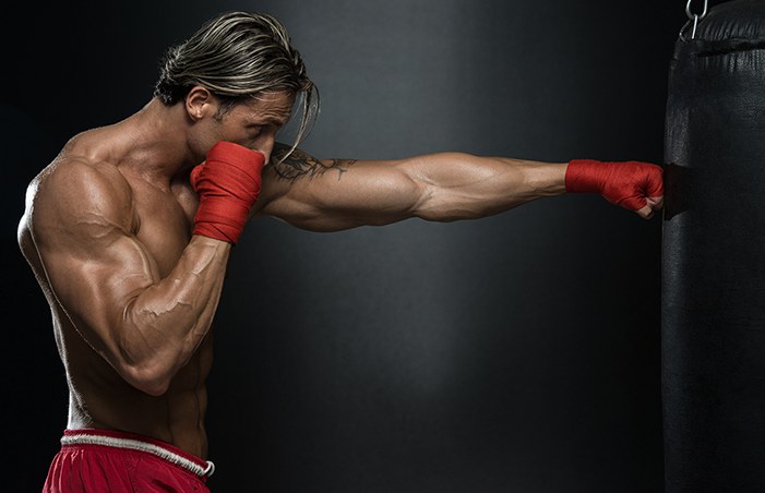 A boxer with red hand wraps punching a black heavy bag against a dark background