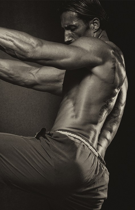 Sepia photo of a muscular fighter with his arms on a heavy bag and one knee raised